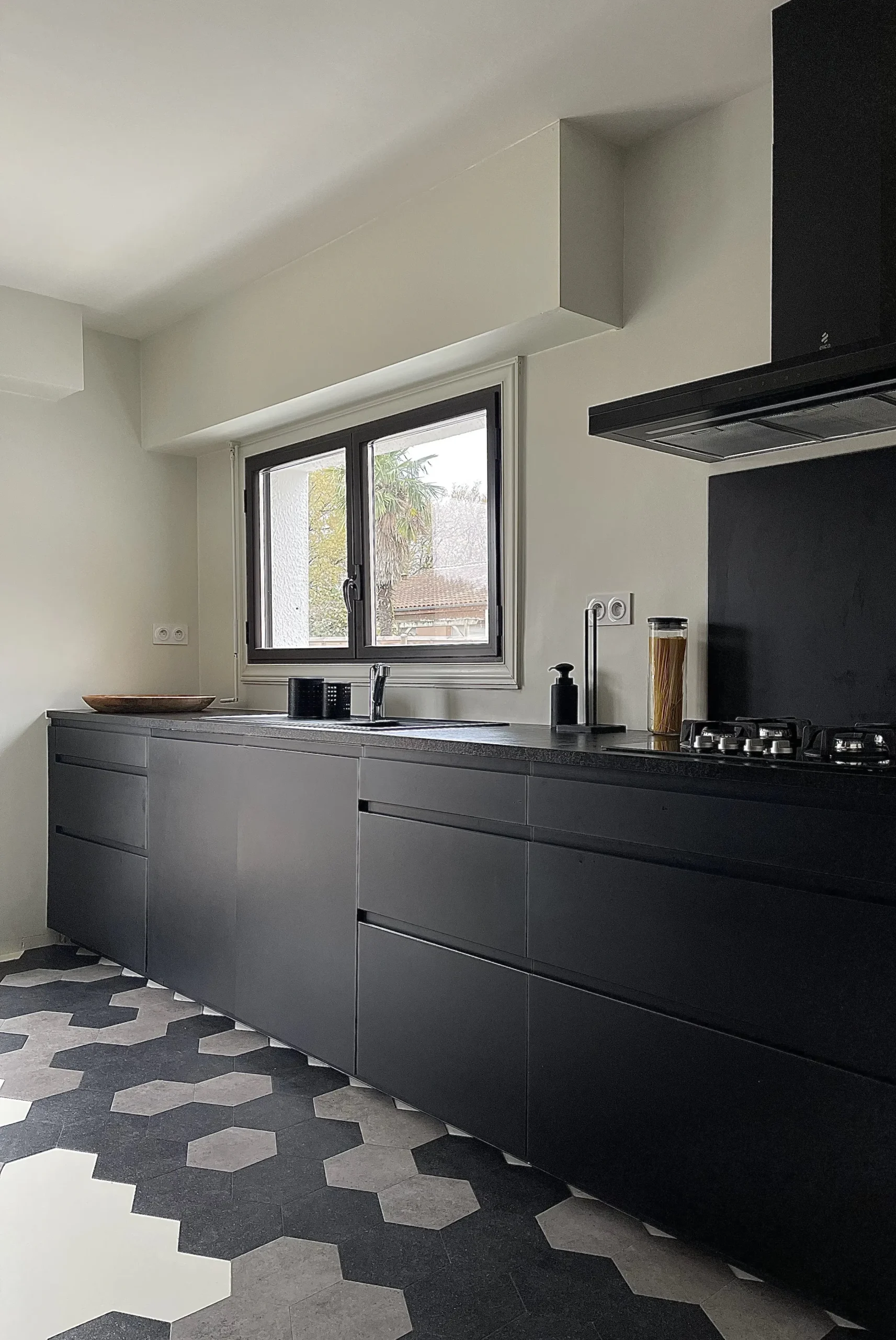 Cuisine au style industriel avec armoires noires, sol à motifs géométriques en noir et blanc, et touches de design industriel, complétée par des accessoires minimalistes et un éclairage d'ambiance.